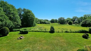 A lush green landscape with a clear blue sky, a thatched roof structure, and a well-maintained grassy area with a fence. - Buchfink, Deutschland (Prerow)