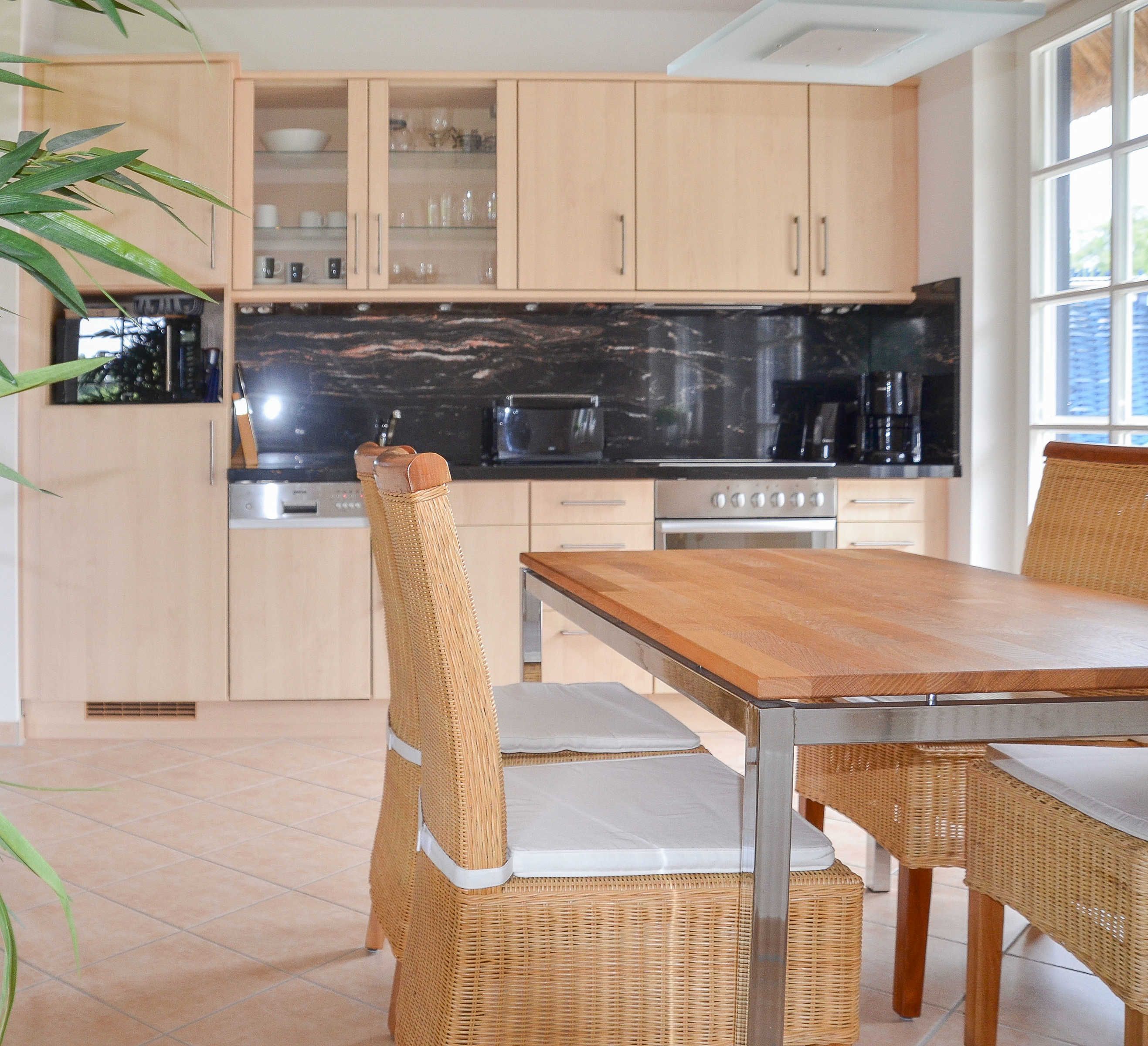 Une cuisine avec des meubles en bois, un plan de travail noir et un coin repas comprenant des chaises en osier et une table en bois.