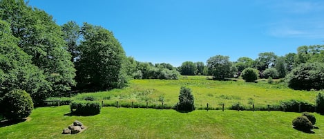 A lush green landscape with a clear blue sky, a thatched roof structure, and a well-maintained grassy area with a fence.