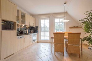 A kitchen with a dining area, large windows, and a plant.