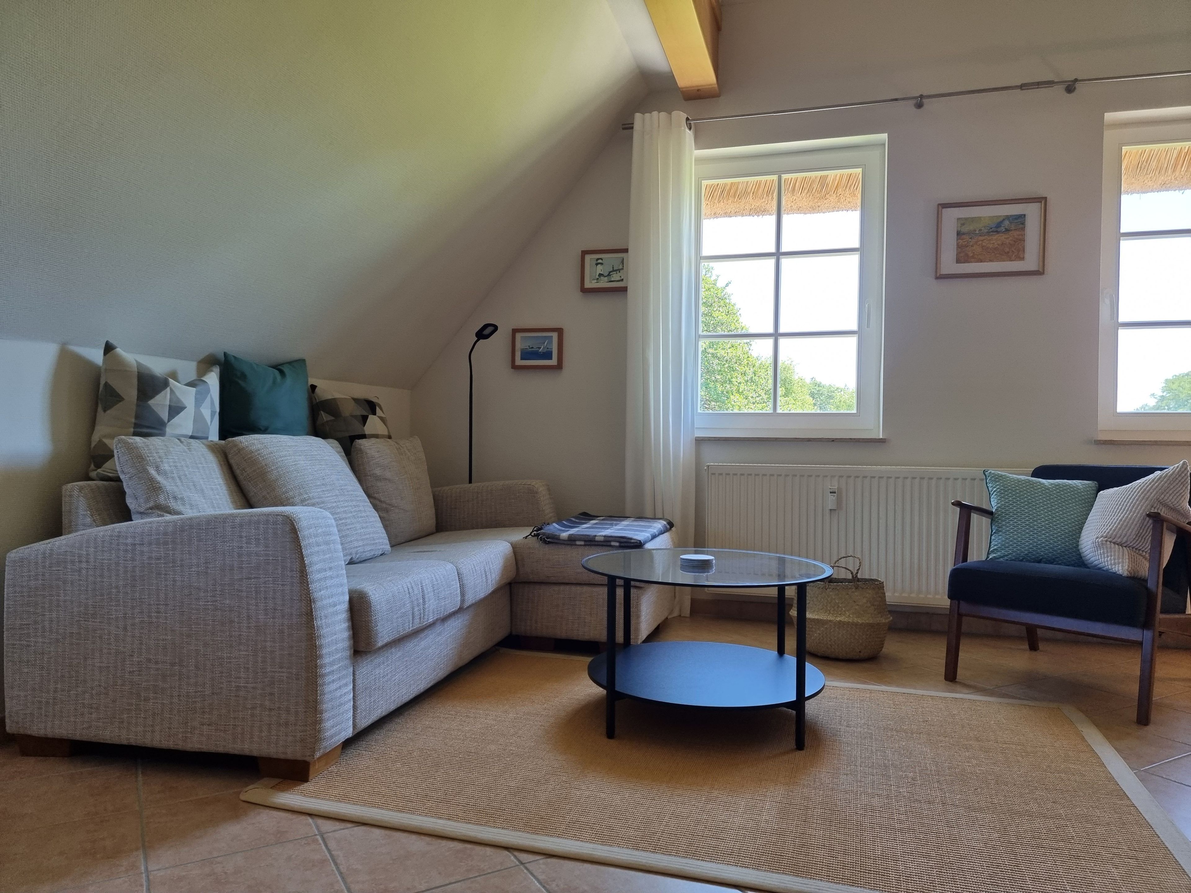 Un salon comprenant un canapé, une petite table ronde, un fauteuil, un radiateur et une fenêtre donnant sur un espace verdoyant.