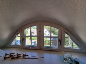 A room with a sloped ceiling, large arched windows, and a glass table.