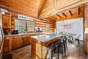 Une cuisine de style rustique, avec un îlot central, des armoires en bois et un panneau indiquant « THÉ SUCRÉ ».