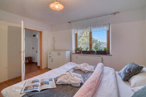 Ein Schlafzimmer mit Bett, einem Fenster mit Vorhängen, einem Heizkörper und einer Tür zu einem Badezimmer.