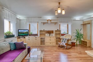 Ein Wohnzimmer mit einer Couch, Fernseher, Holzschränken, einem Schaukelstuhl und einem Blumentopf.