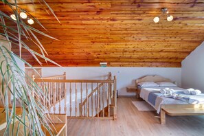 A wooden ceiling with hanging lights, a bed with a wooden headboard, a small bedside table, and a staircase with a wooden railing.