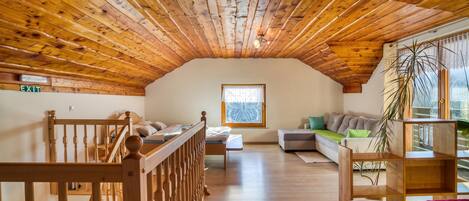A wooden interior with a sloped ceiling, a sofa, a bed, and a window with a view.
