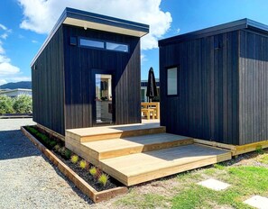 A modern two-story house with a wooden deck and a small garden area. - Oasis in the Heads (Mangawhai)
