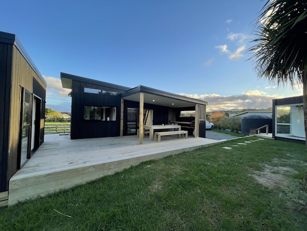 A modern house with a covered patio, a wooden deck, and a view of the countryside. - Oasis in the Heads (Mangawhai)