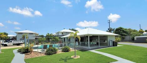 A residential area with a swimming pool, a covered patio, and a well-maintained lawn.