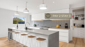 Eine moderne Küche mit Kochinsel, Barhocker, Pendelleuchten und einem Schild mit der Aufschrift 'PAY 2 STAY 3'.