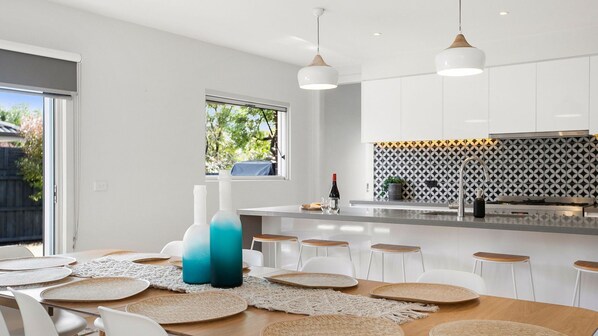 Een moderne keuken met witte kastjes, een decoratieve spatwand en een eetgedeelte met een houten tafel en witte stoelen.