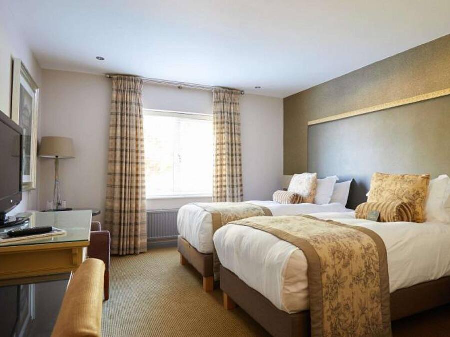 Ett hotellrum med två sängar, ett skrivbord med en dator, en tv och ett fönster med gardiner.