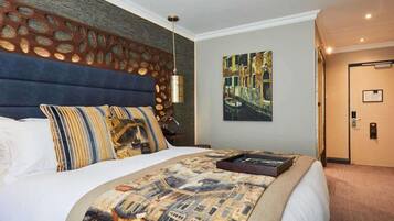 A hotel room with a large bed, a headboard with circular patterns, a painting on the wall, and a door with a handle.