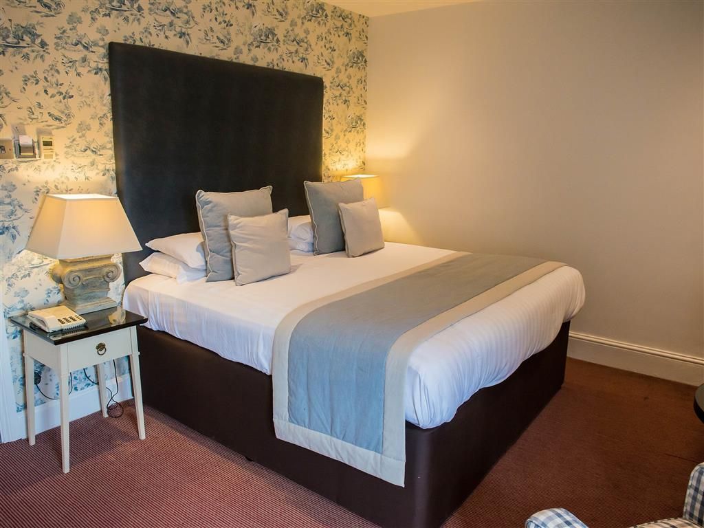 A neatly made bed with a dark headboard, two bedside lamps, and a small bedside table with a lamp and a telephone.