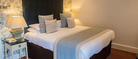 Una cama bien hecha con un cabecero oscuro, dos lámparas de noche y una mesita de noche con lámpara y teléfono.