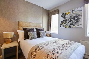 Ein Hotelzimmer mit einem großen Bett, einem Nachttisch mit Lampe, einem Wandbild und einem Vorhangfenster.