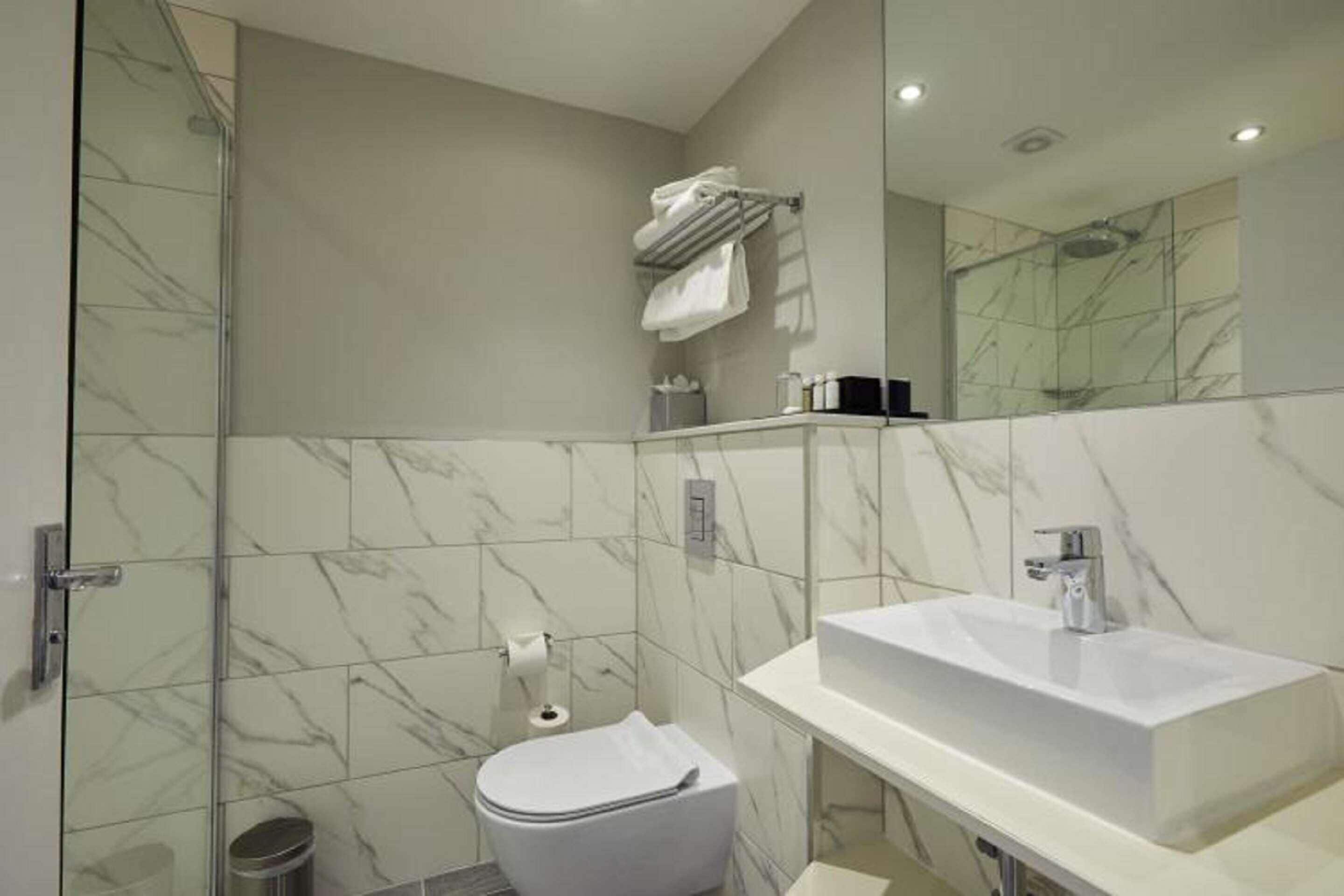 A modern bathroom with a glass shower enclosure, a white toilet, a white sink, and a marble-tiled wall.