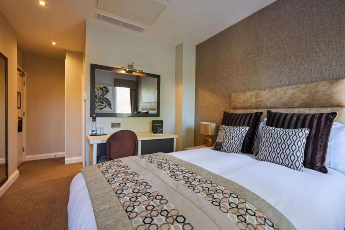 Een hotelkamer met een groot bed, een bureau met stoel, een spiegel en een hoofdbord met decoratieve kussens.