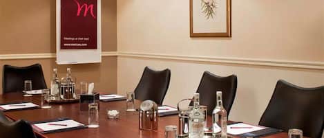 Un salón de conferencias con una larga mesa, sillas y diversos objetos como botellas y una bandeja.