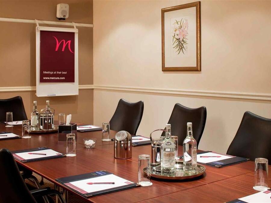 Un salón de conferencias con una larga mesa, sillas y diversos objetos como botellas y una bandeja.