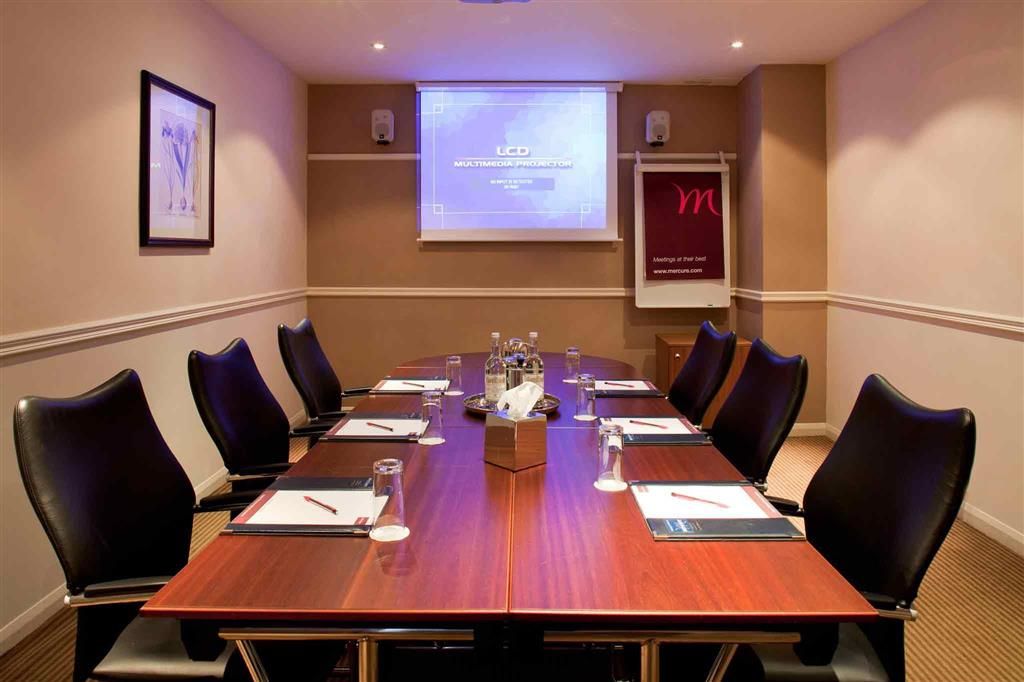 A conference room with a long table, black chairs, water bottles, and a presentation screen.