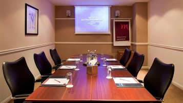 A conference room with a long table, black chairs, water bottles, and a presentation screen.