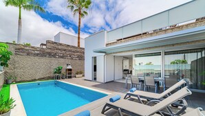 A modern outdoor pool area with lounge chairs, a stone wall, and a glass-enclosed patio.
