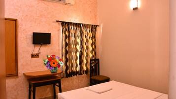 Habitación de hotel con cama, escritorio y silla, televisión montada en la pared y ventana con cortinas.