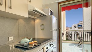 A modern kitchen with a built-in oven, a microwave, and a refrigerator. There is a window with a view of a balcony and buildings. - N&J - SUNRISE TERRACE - Close sea - Terrace 30m² (Niza)