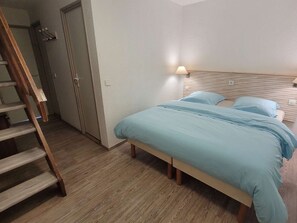 A bedroom with a bed, a nightstand, a lamp, and a wooden floor.