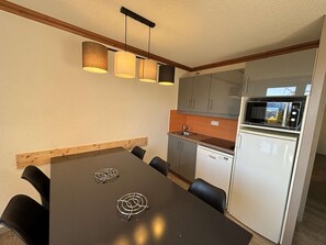 A compact kitchen with a dining area, featuring a microwave, dishwasher, and a wooden dining table with chairs. - Duplex 2BR Ski-In/Out, Pool & Sauna Access, Sleeps 6, Close to Shops - Alpe d'Huez (Huez)