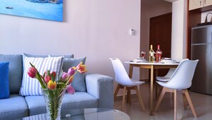Una sala moderna con un sofá, una mesa de centro de vidrio y una mesa de comedor preparada para dos.