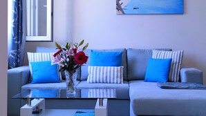 Una sala de estar moderna con un sofá gris, cojines azules, una mesita de centro de cristal y un jarrón con flores.