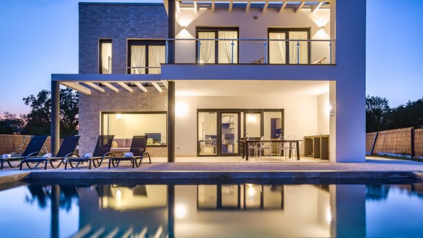 Ein modernes, zweistöckiges Haus mit Schwimmbecken im Vordergrund, inklusive einer Terrasse mit Liegestühlen und Essbereich.