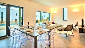 Ein modernes Wohnzimmer mit einem Glastisch, transparenten Stühlen, einer Couch und einem Fernsehschrank.
