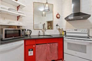 Cocina con armarios blancos, encimera roja, microondas, estufa, fregadero y una lámpara colgante.