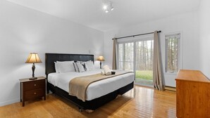 A bedroom with a large bed, two bedside tables, a wooden dresser, and a window with curtains.