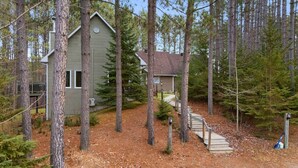 A cabin surrounded by tall trees, with a wooden staircase leading to the entrance.