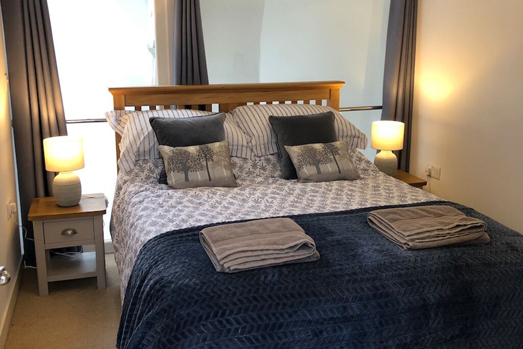 Un lit bien fait, avec une couvre-lit à motifs, deux oreillers et deux serviettes pliées, le tout posé sur une tête de lit en bois.