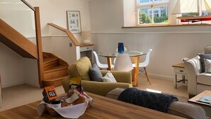 A modern living room with a wooden staircase, a dining area with a glass table, and a sofa with cushions. - Luxury duplex flat in central Falmouth with parking (Falmouth)