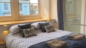 A neatly made bed with a patterned bedspread, pillows, and two folded towels. - Luxury duplex flat in central Falmouth with parking (Falmouth)