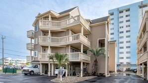 A multi-story hotel with balconies, a parking area, and a neighboring building. - Salty Hammocks B1 (Carolina Beach)