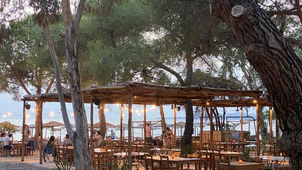 An outdoor dining area with wooden tables and chairs, string lights, and umbrellas. - Villa Emerald - brand new house few minutes from the beach (Nikiti, Sithonia)