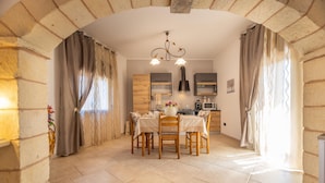 A dining area with a table set for four, a chandelier, and a kitchen in the background.
