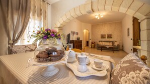 A cozy room with a dining table set for tea, a decorative glass dome over cookies, and a floral centerpiece.