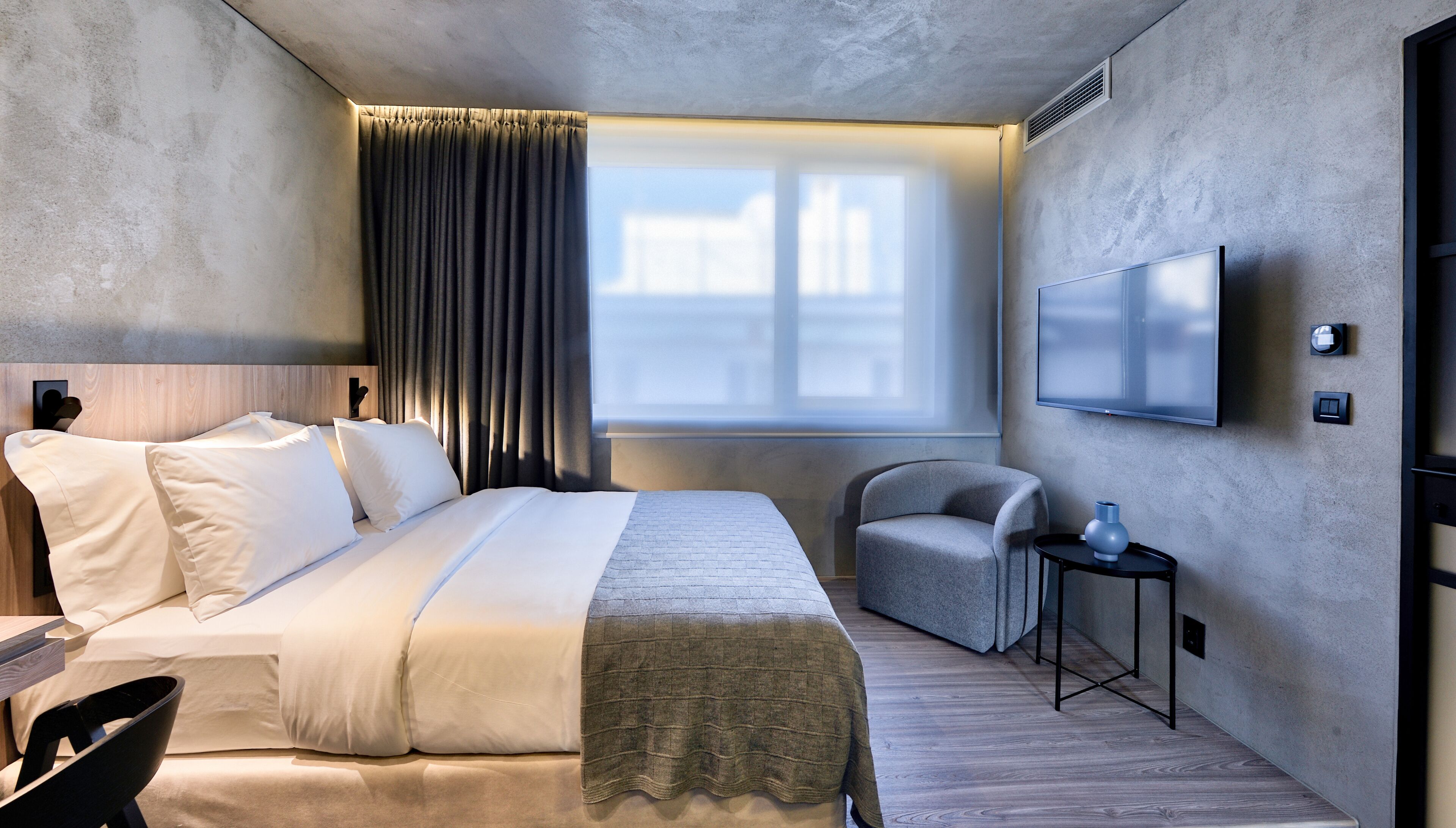 Een hotelkamer met een bed, een stoel, een televisie en een raam met gordijnen.