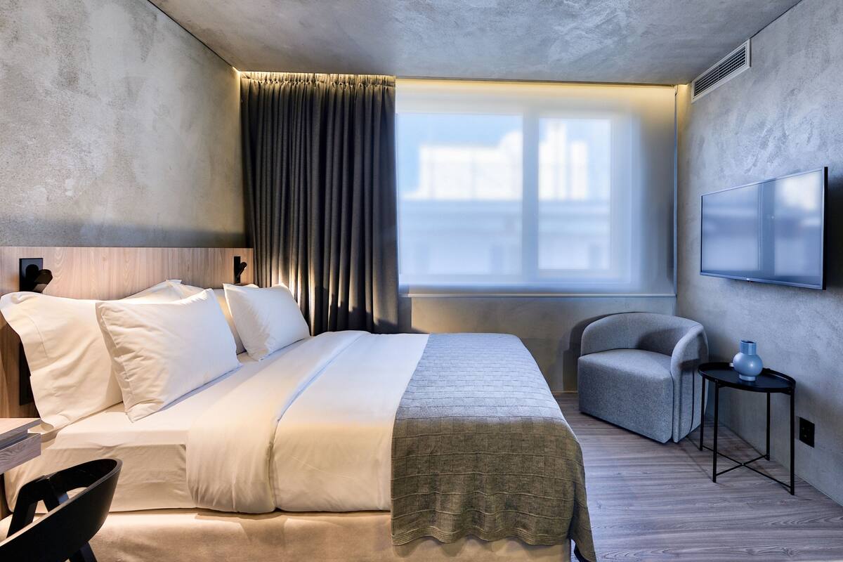 A hotel room with a bed, a chair, a TV, and a window with curtains.