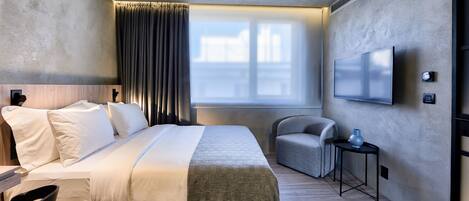 A hotel room with a bed, a chair, a TV, and a window with curtains.