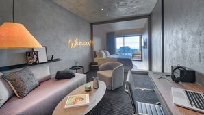 Una habitación de hotel moderna con sofá, sillón, mesitas de noche, una computadora portátil y vistas a la ciudad.
